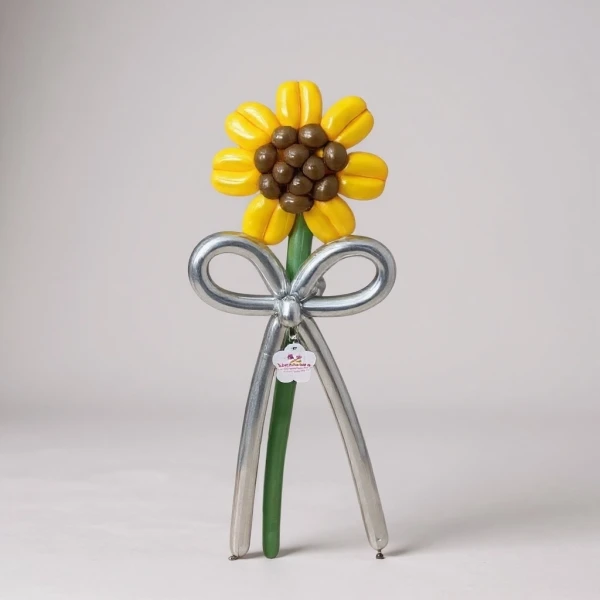 A balloon sunflower with yellow petals and a brown center, a silver bow and stem, on a light background.