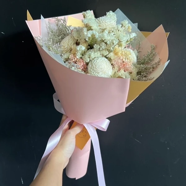 Bouquet of ivory and pastel dried flowers wrapped in pink paper with a ribbon.