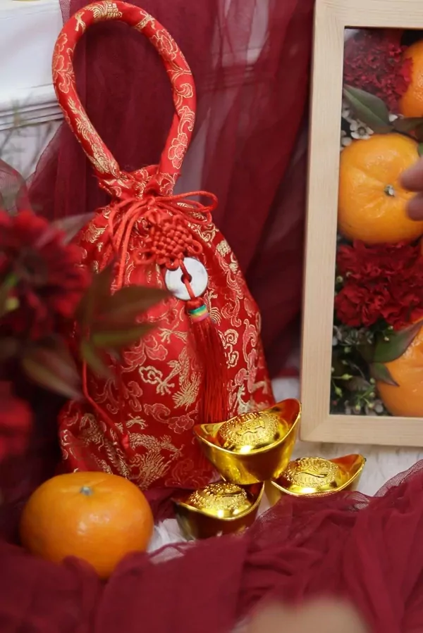 Red Chinese New Year bag with golden dragon pattern and oranges, gold ingots, and flowers.