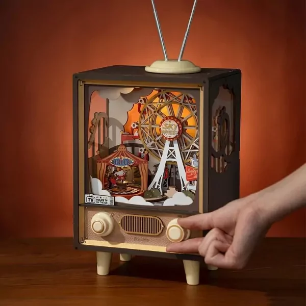DIY rotating circus music box in vintage TV shape, with hand turning a knob.