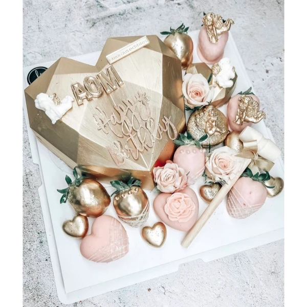 Gold heart chocolate gift box with smashable center, decorated strawberries, and cupid figures.