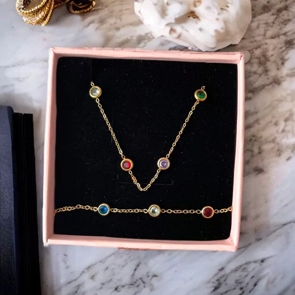 Gold necklace and bracelet set with multi-colored gemstones in a pink box.