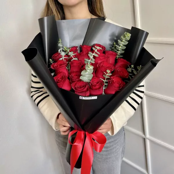 Woman holding a bouquet of 18 red roses wrapped in black paper and tied with a red ribbon.
