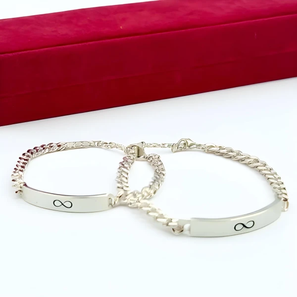 Silver infinity charm bracelets for couples on a white surface with a red box behind them.