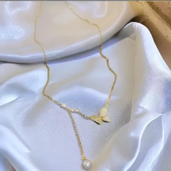 Gold necklace with butterfly pendant, pearls, and delicate chain on white satin.