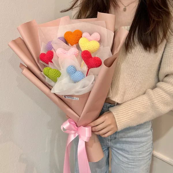 Crocheted heart bouquet in mixed colors, wrapped in pink paper and tied with a pink bow.