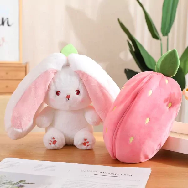 A plush strawberry toy sits next to a white plush bunny with pink ears and paws.