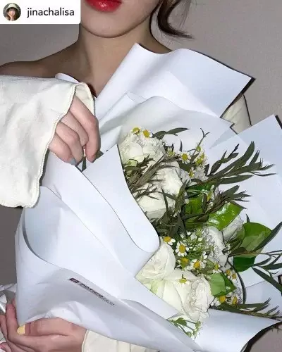 Woman holding a white rose and daisy bouquet wrapped in white paper.