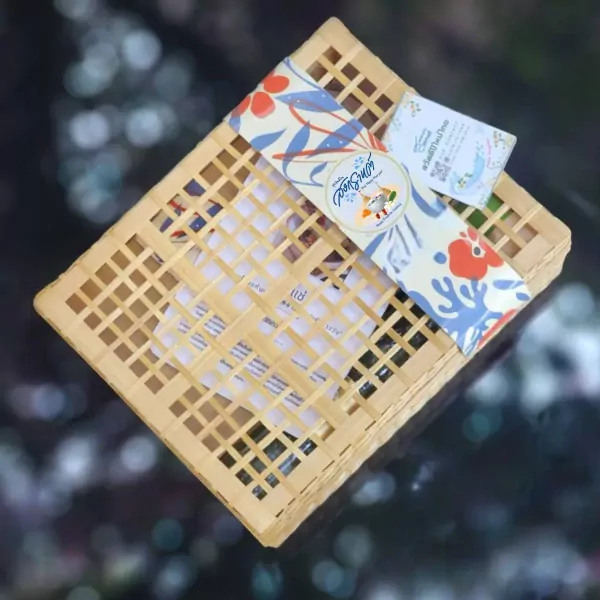 A woven bamboo box filled with Khao Chae ingredients and topped with a floral ribbon and label.