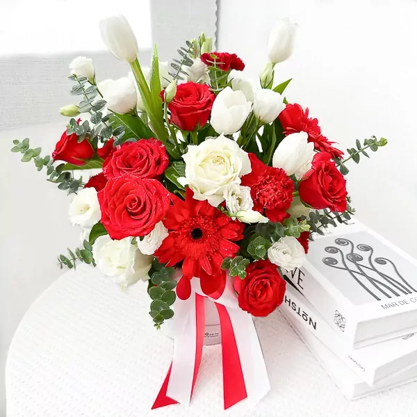 A floral arrangement in a white box with red and white roses, tulips, gerberas, carnations, lisianthus, and eucalyptus.