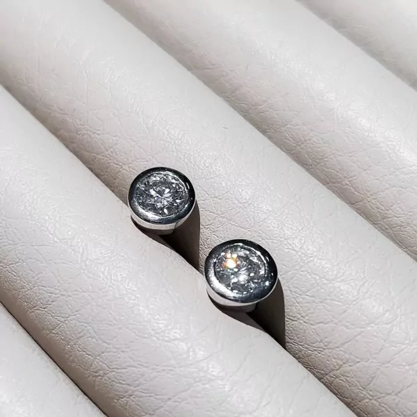 Pair of 0.5-carat round-cut moissanite diamond stud earrings set in silver on a textured white surface.
