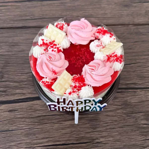 Miniature strawberry yogurt and white chocolate cake with pink frosting roses, white chocolate squares, and a "Happy Birthday" topper.