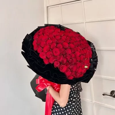 99 red roses arranged in a heart shape, a large bouquet with black wrapping and a red bow.