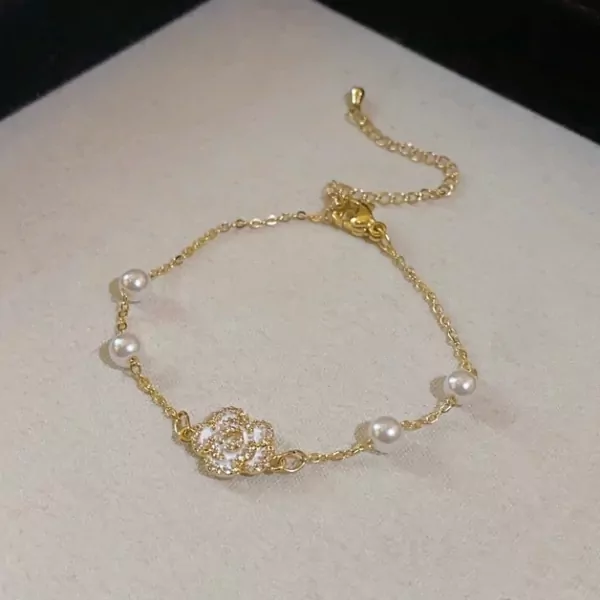 Gold bracelet with a white floral charm and pearls.