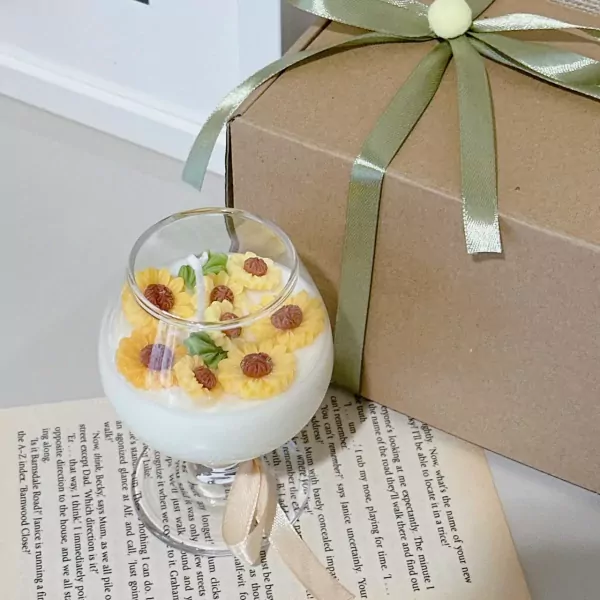 Sunflower scented candle in a wine glass, topped with tiny sunflower candles. Gift box in background.