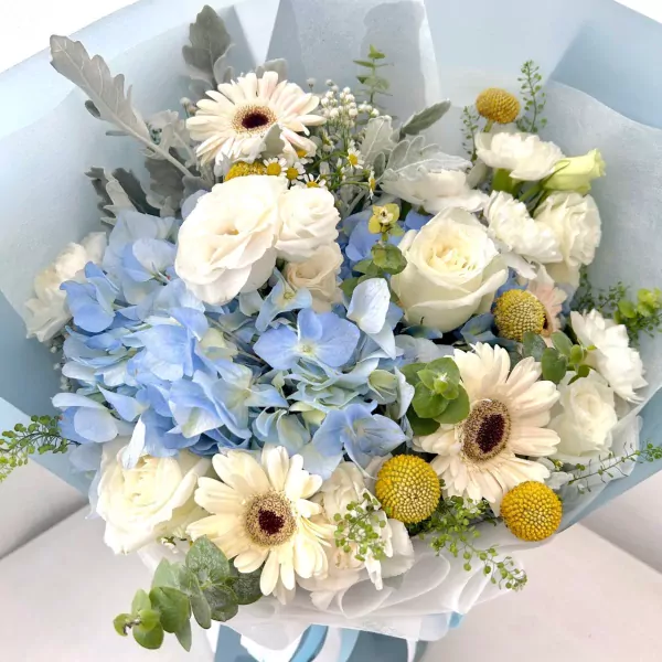 Blue hydrangeas, white roses, and gerbera daisies in a bouquet wrapped in blue and white paper.