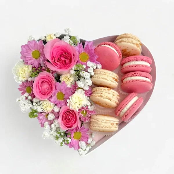 Heart-shaped box with pink roses, daisies, and pink and vanilla macarons.
