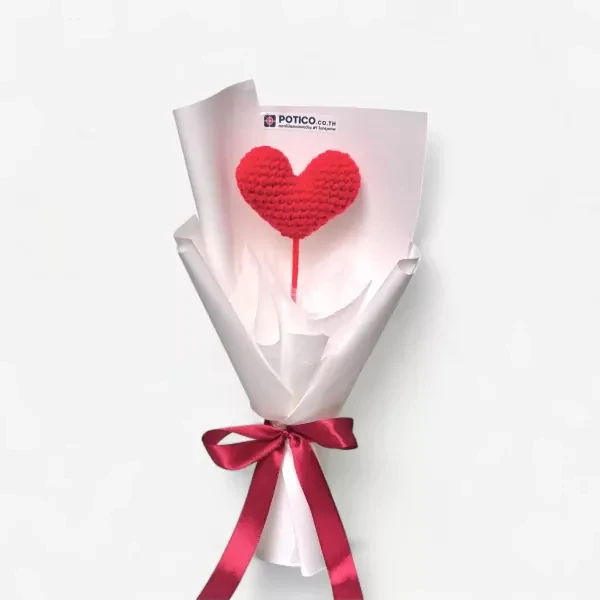 Crocheted red heart on a stick in a white paper bouquet with a red ribbon.