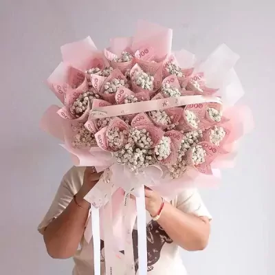 A bouquet of rose-shaped banknotes and baby's breath, wrapped in pink paper.