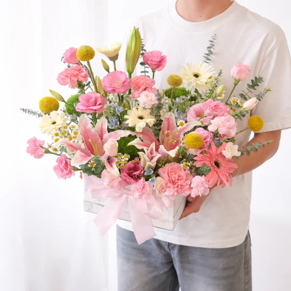 Pink lilies, gerberas, carnations, and yellow button mums in a white box with a pink bow.