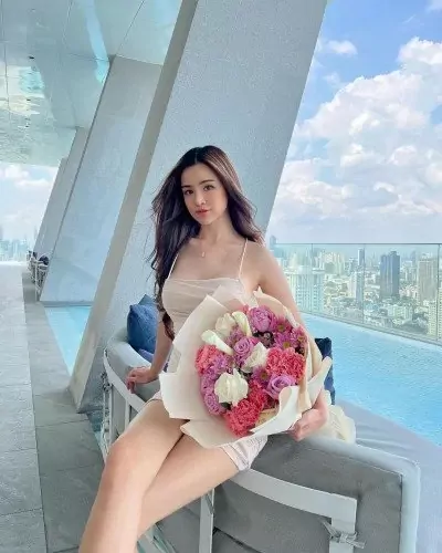 Woman holding a bouquet of pink and purple flowers by a pool with a city view.