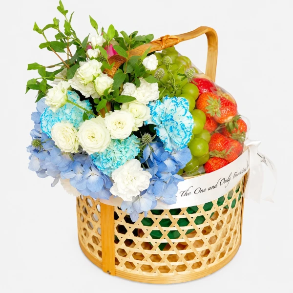 Woven basket with strawberries, green apples, and a blue and white flower arrangement.