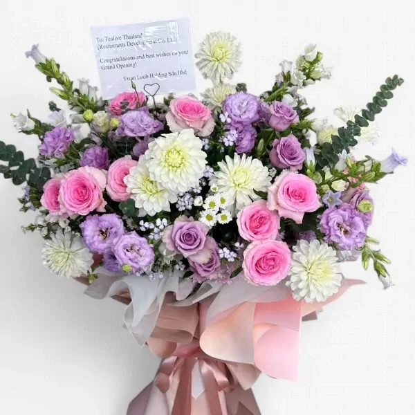 A floral stand with pink roses, purple lisianthus, white dahlias, and green foliage, wrapped in pale pink and white paper.