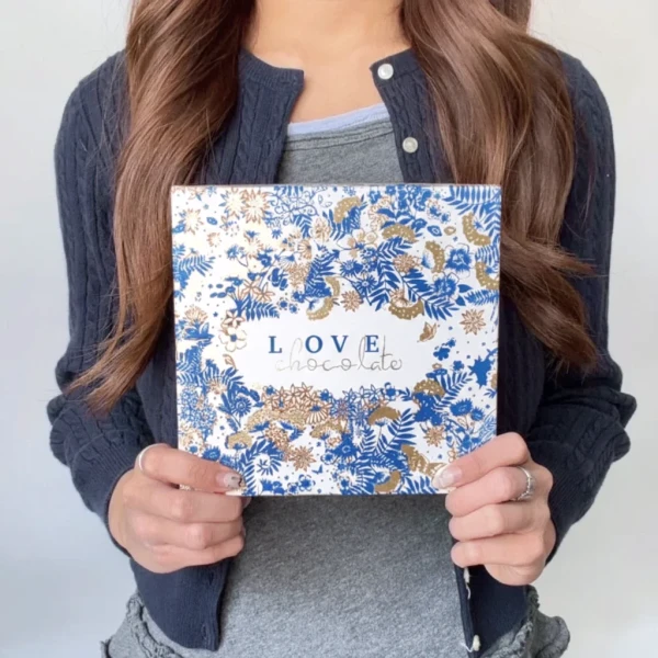 Woman holding a white and blue floral box with "Love Chocolate" written on it.