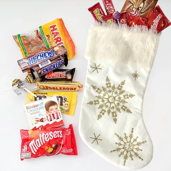 White Christmas stocking filled with candy, including Kit Kat, Snickers, Mars, and Maltesers.
