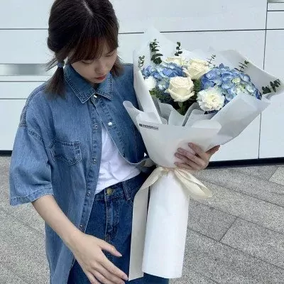 Woman in denim holding a white and blue bouquet of roses, hydrangeas, and eucalyptus.