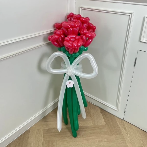 Giant red rose balloon bouquet with white balloon ribbon tied around green balloon stems.