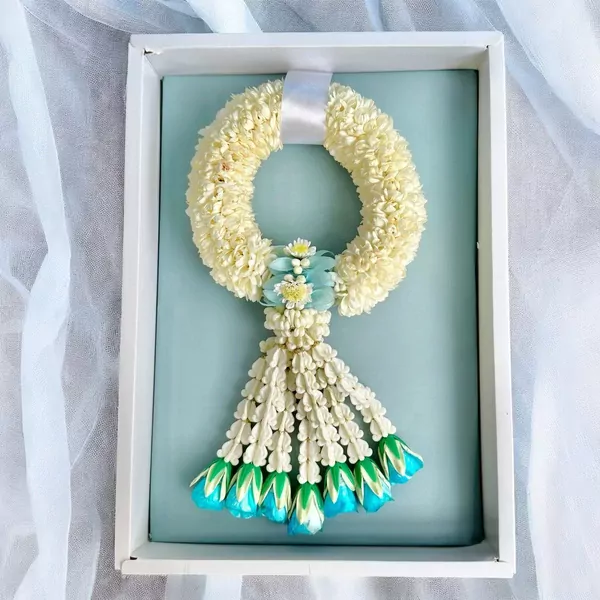 A circular white jasmine garland with light blue accents in a white gift box.