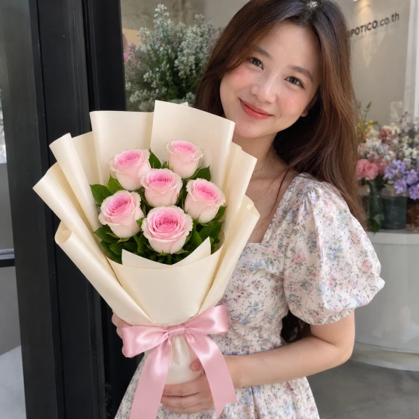 Bouquet of six pink roses, wrapped in white paper, tied with a pink ribbon.