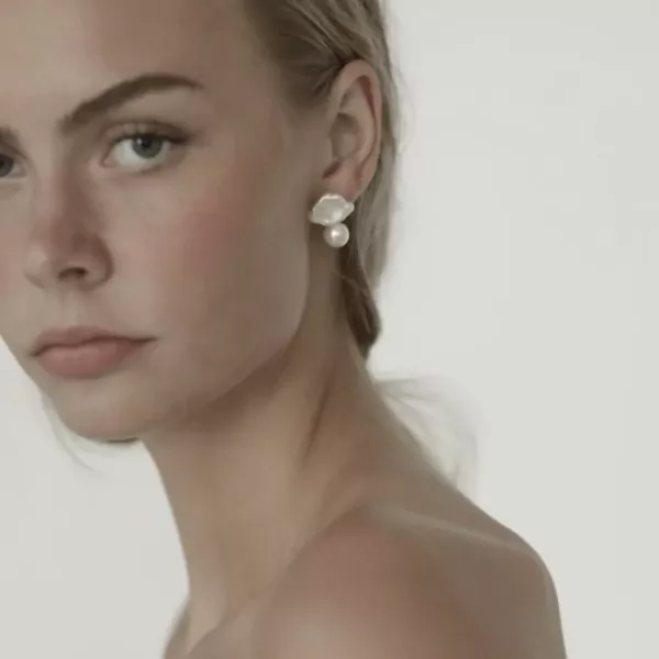 Model wearing pearl droplet earrings, close-up of face and shoulders.