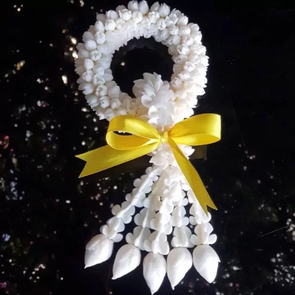 White jasmine malai garland with yellow bow against a dark, speckled background.