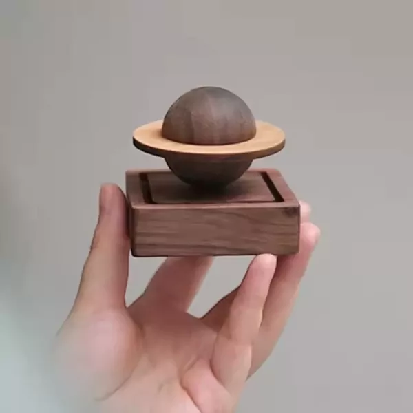 Hand holding a wooden planet oil diffuser with rings, on a wooden base.