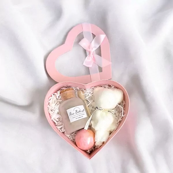 Pink heart-shaped spa gift box containing rose bath salts, a bath bomb, and fluffy white towel artfully arranged as a teddy bear.