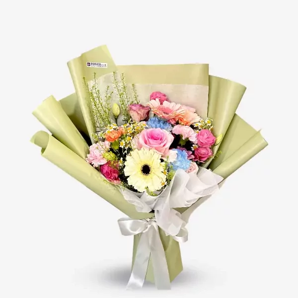 A vibrant bouquet of pink roses, gerberas, blue carnations, and yellow blooms wrapped in light green paper with a white ribbon.