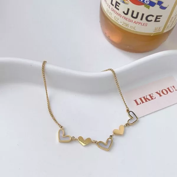 Gold necklace with five alternating white and gold heart charms on a white cloth background.