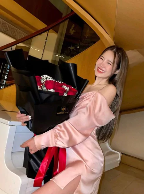 Woman in pink dress smiles holding a bouquet of 24 red roses.