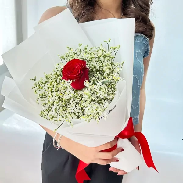 Red rose bouquet with white limonium, wrapped in white paper and tied with a red ribbon.