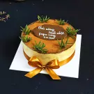 Tiramisu cake decorated with grass, brown frosting, and a gold ribbon.
