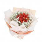 Strawberry and baby's breath bouquet wrapped in peach and white paper, tied with a ribbon.