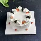 Round white cake with cream swirls, strawberries, blueberries, and raspberries.