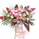 Pink floral arrangement with roses, carnations, and gerbera daisies on a wooden stand.