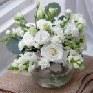 White flowers in a glass vase, featuring roses, carnations, and lisianthus.