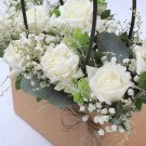 White roses, baby's breath, and eucalyptus in a brown box with twine.