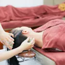 Person receiving a herbal hair wash with green herbal massage balls on a massage table.