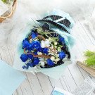 Blue roses, white accent flowers, and greenery in a bouquet, with a black and white checkered hat on top.