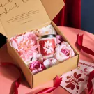 Gift box with a scented candle, pink flowers, and ribbons.